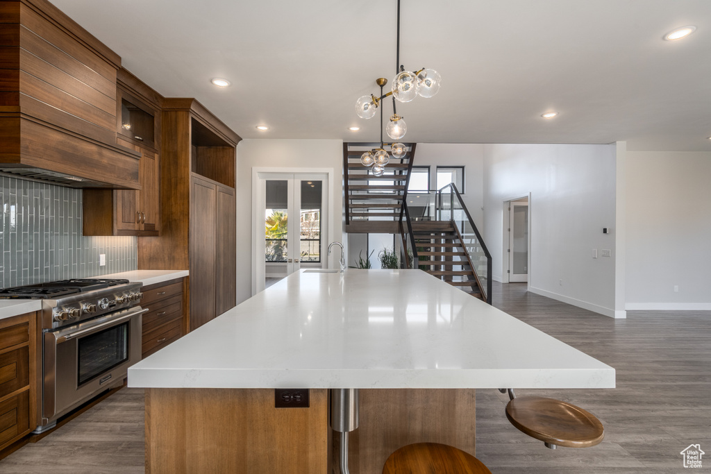 Kitchen featuring high end stainless steel range, dark wood-type flooring, light countertops, a spacious island, and decorative backsplash