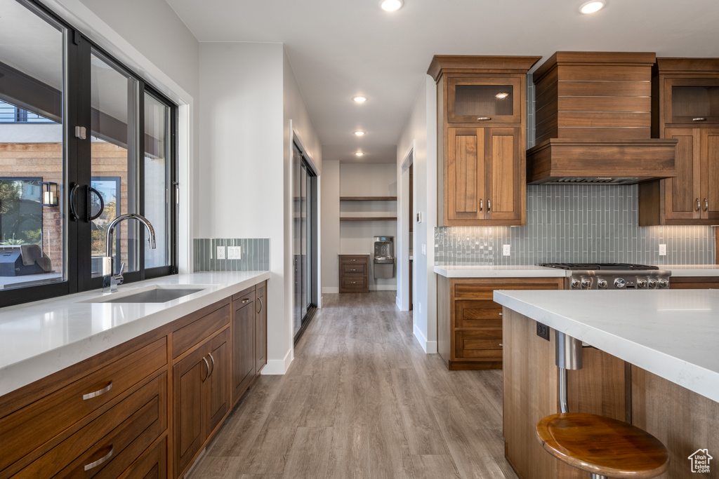 Kitchen with decorative backsplash, light wood finished floors, recessed lighting, brown cabinetry, and glass insert cabinets