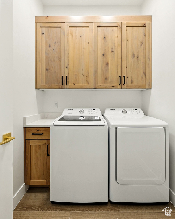 Laundry area featuring washing machine and dryer, cabinet space, and wood finished floors