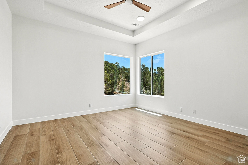 Empty room with light wood-type flooring, a raised ceiling, and ceiling fan