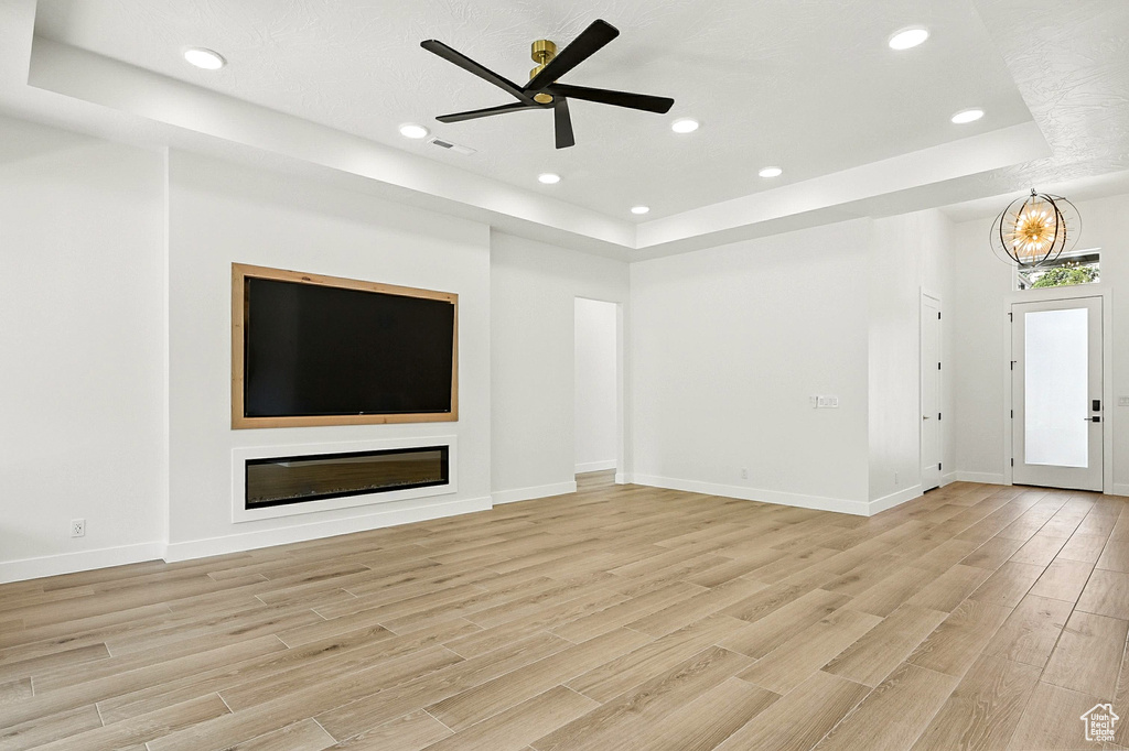 Unfurnished living room featuring a raised ceiling, light wood-style flooring, a ceiling fan, and recessed lighting