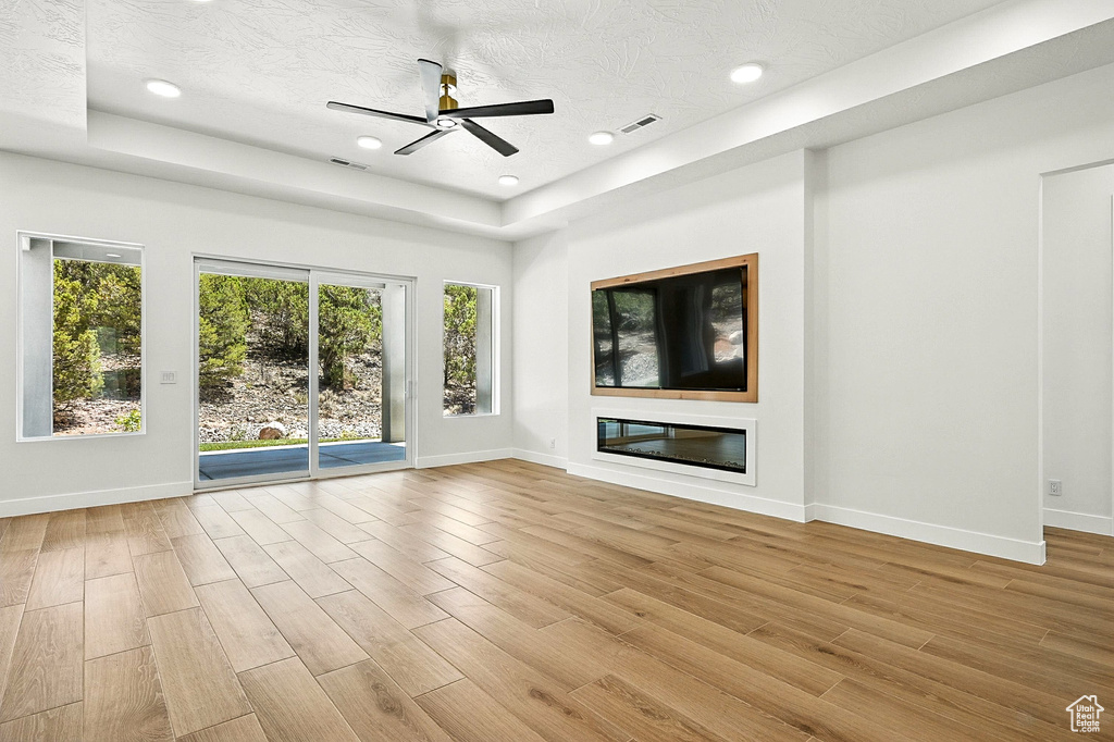 Unfurnished living room with a raised ceiling, light wood finished floors, a ceiling fan, recessed lighting, and a textured ceiling