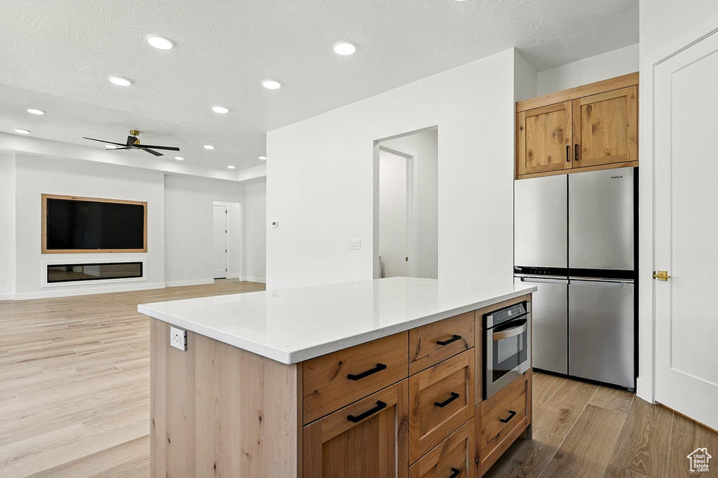 Kitchen with freestanding refrigerator, light wood-type flooring, a ceiling fan, recessed lighting, and light countertops