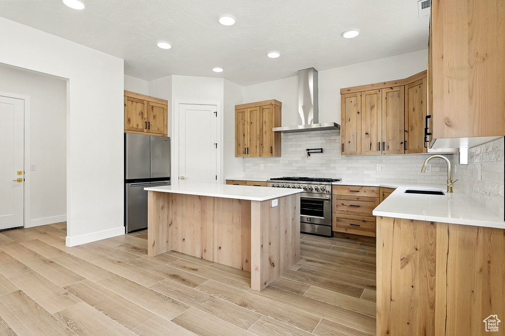 Kitchen featuring stainless steel appliances, wall chimney exhaust hood, a kitchen island, tasteful backsplash, and light countertops