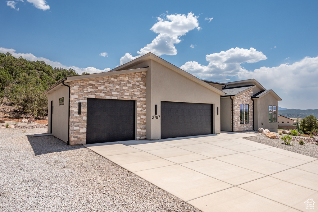 View of front of property featuring a garage, stucco siding, stone siding, driveway, and a mountain view