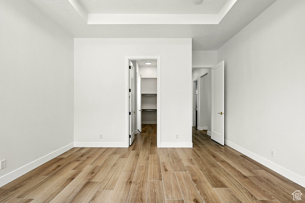 Unfurnished bedroom featuring light wood-style flooring, a walk in closet, and a raised ceiling