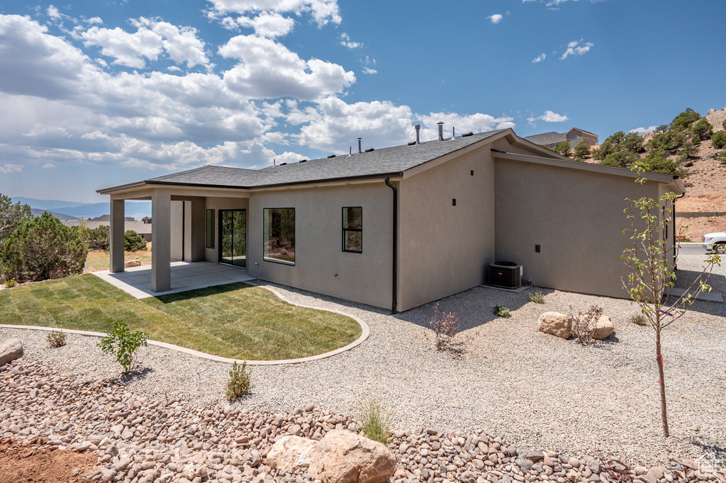 Back of property featuring a patio, a lawn, roof with shingles, and stucco siding