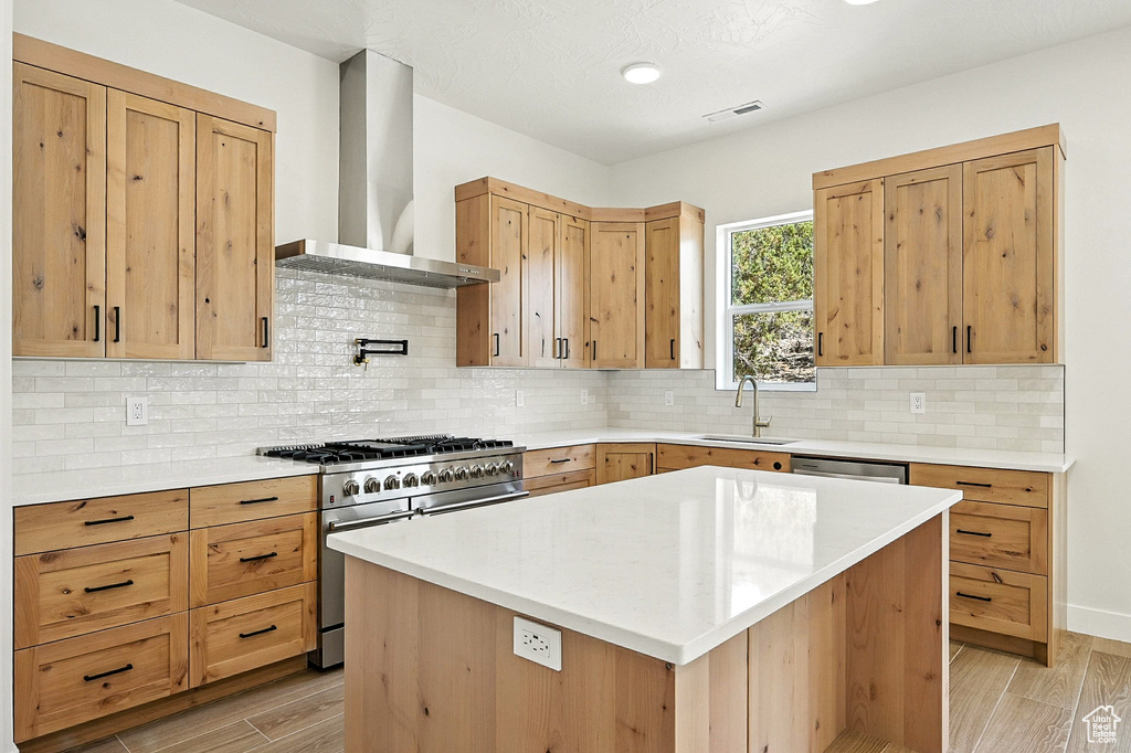 Kitchen featuring high end range, wall chimney range hood, backsplash, light wood-style flooring, and a kitchen island
