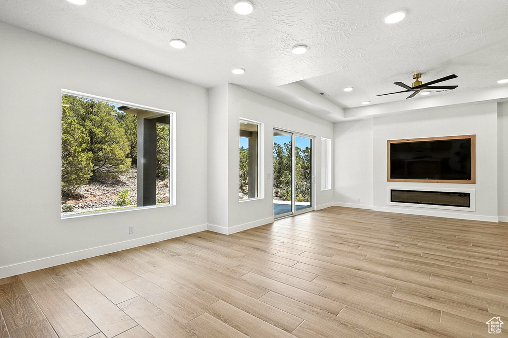 Unfurnished living room featuring plenty of natural light, light wood-style flooring, recessed lighting, ceiling fan, and a textured ceiling