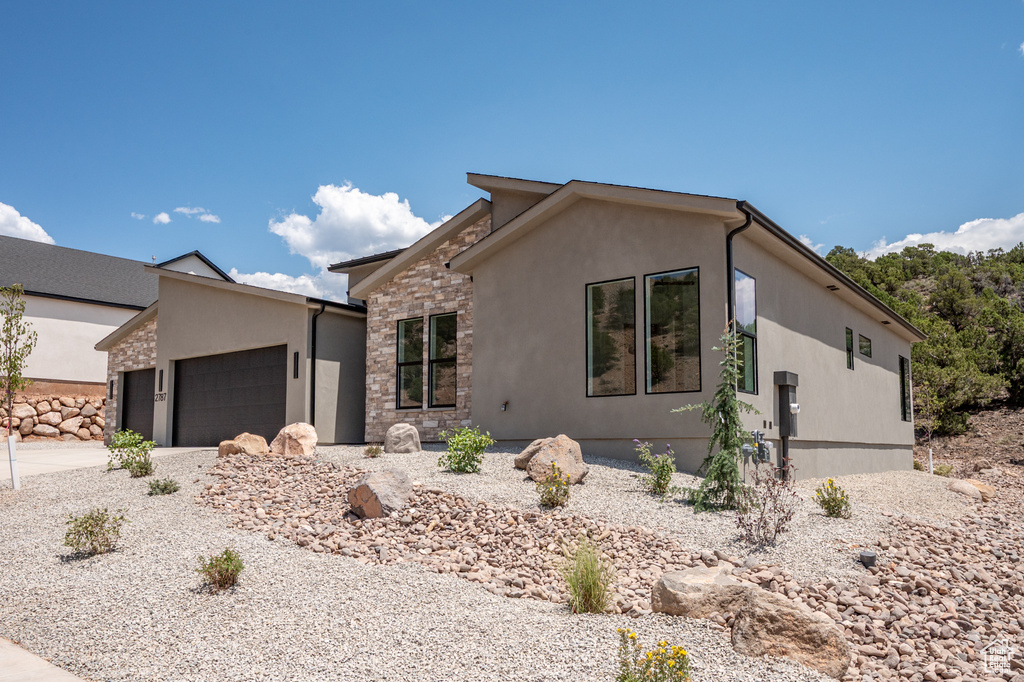 View of front of property with stone siding, a garage, stucco siding, and concrete driveway