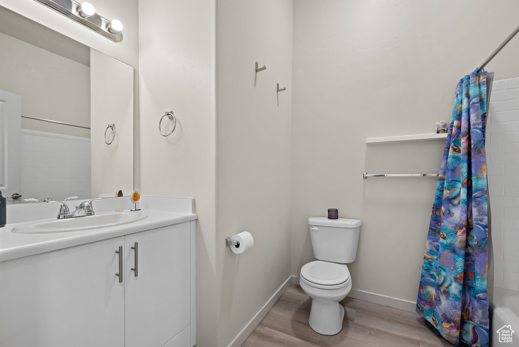 Bathroom with wood finished floors, vanity, and shower / bathtub combination with curtain