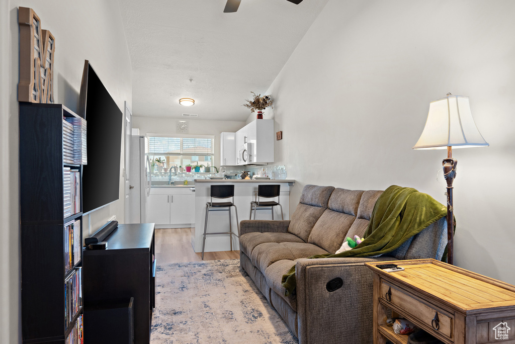 Living room featuring a ceiling fan, light wood-style floors, and lofted ceiling