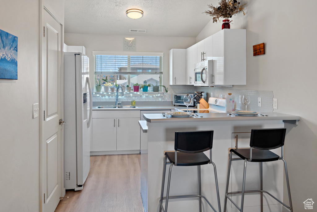 Kitchen featuring a peninsula, backsplash, white appliances, light wood-type flooring, and white cabinets
