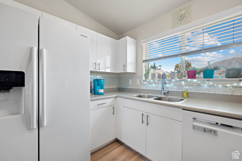 Kitchen featuring white appliances, decorative backsplash, light countertops, and lofted ceiling