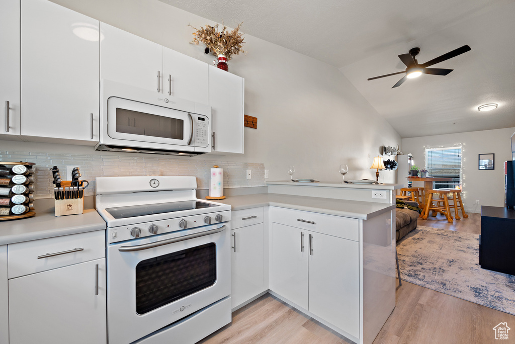 Kitchen featuring white appliances, a peninsula, ceiling fan, decorative backsplash, and light countertops