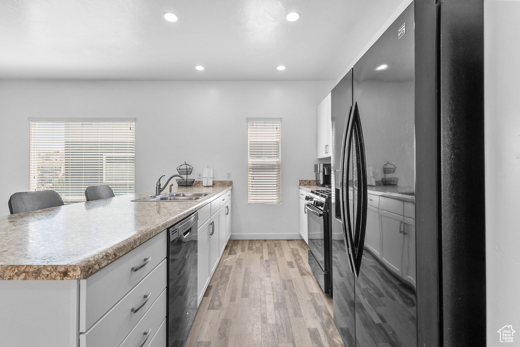 Kitchen featuring black appliances, a peninsula, light wood-style floors, recessed lighting, and light countertops