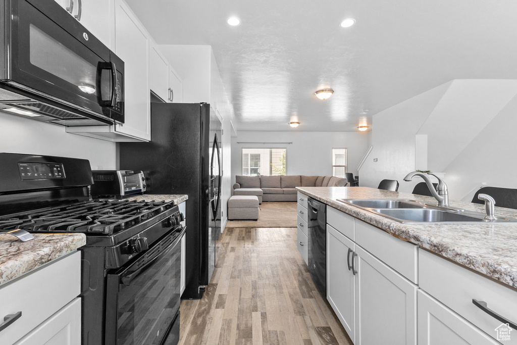 Kitchen featuring black appliances, white cabinetry, light wood finished floors, open floor plan, and light stone counters