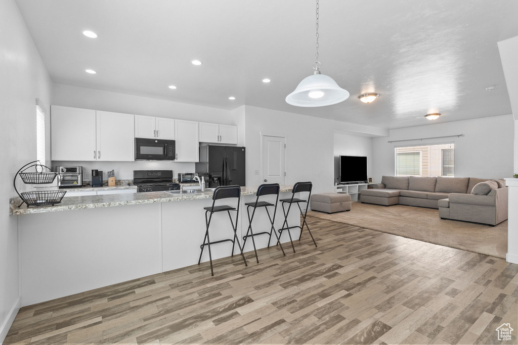 Kitchen featuring white cabinets, black appliances, light wood-type flooring, recessed lighting, and a peninsula