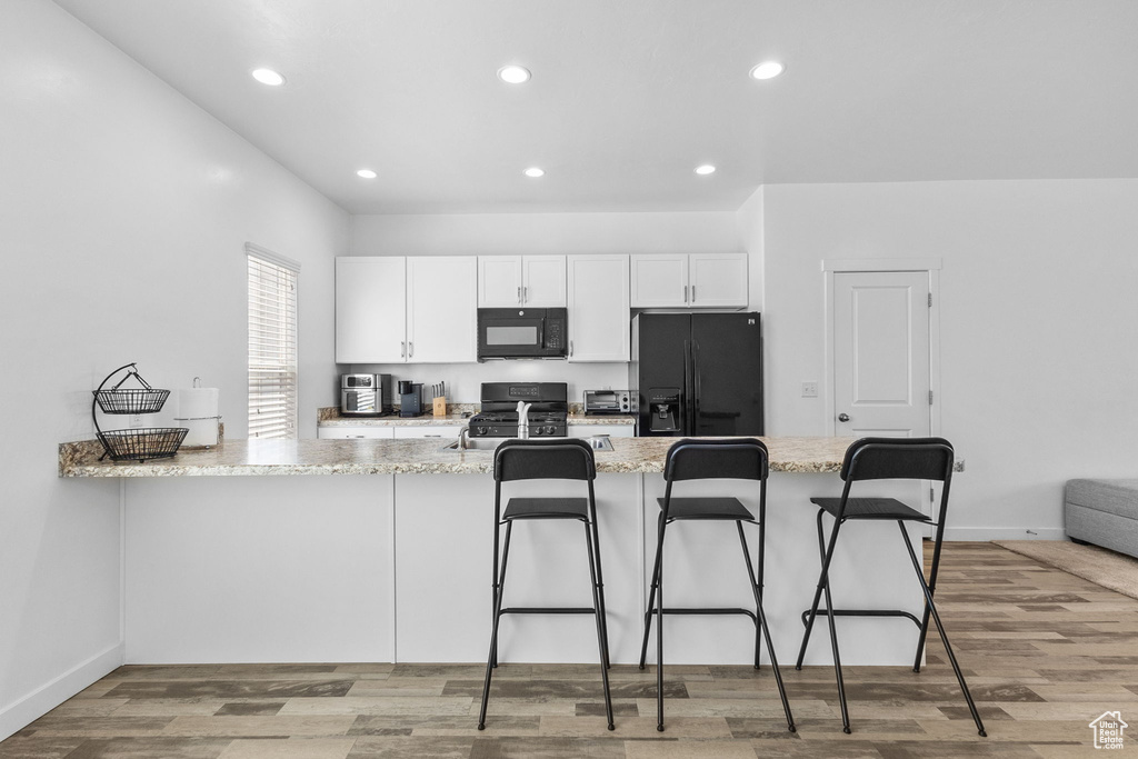 Kitchen with white cabinets, black appliances, a breakfast bar area, light stone countertops, and light wood finished floors