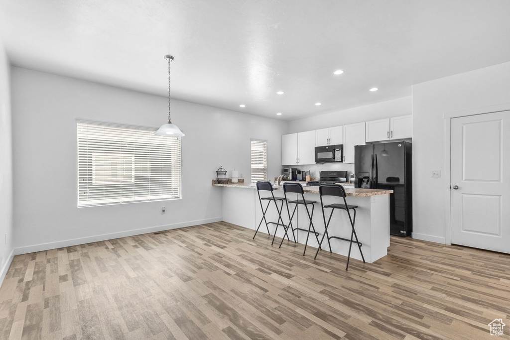 Kitchen featuring light wood finished floors, black appliances, a peninsula, white cabinetry, and recessed lighting