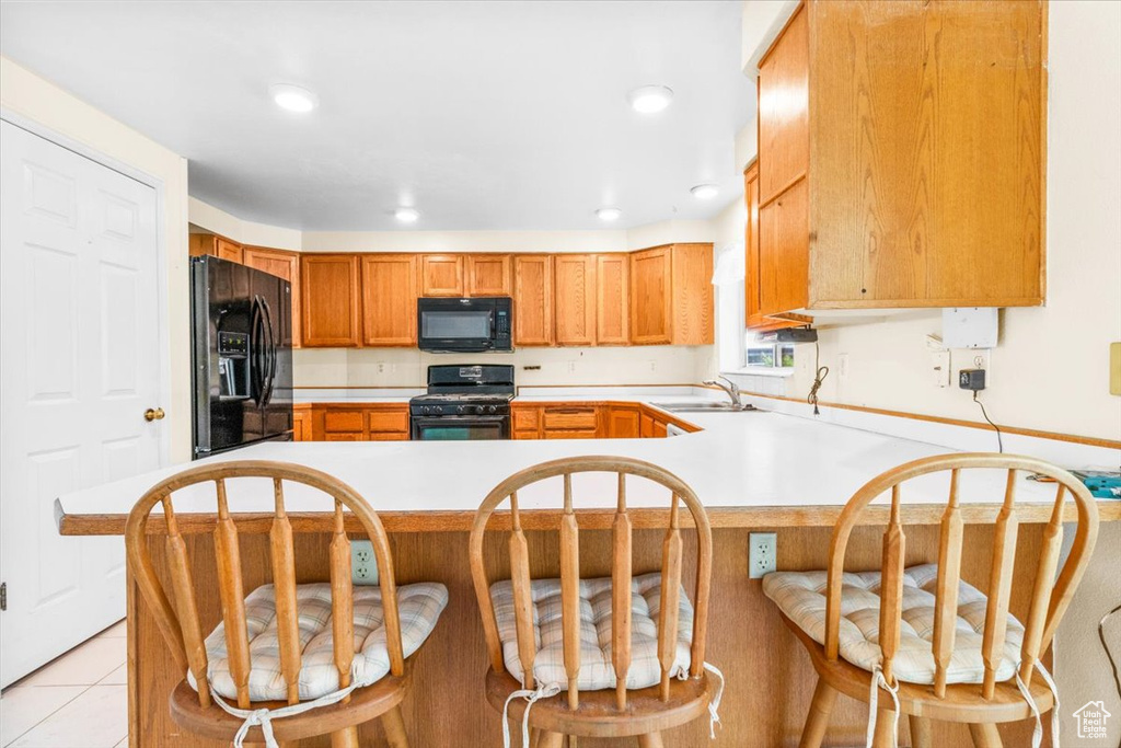 Kitchen featuring black appliances, light countertops, a peninsula, a kitchen bar, and recessed lighting