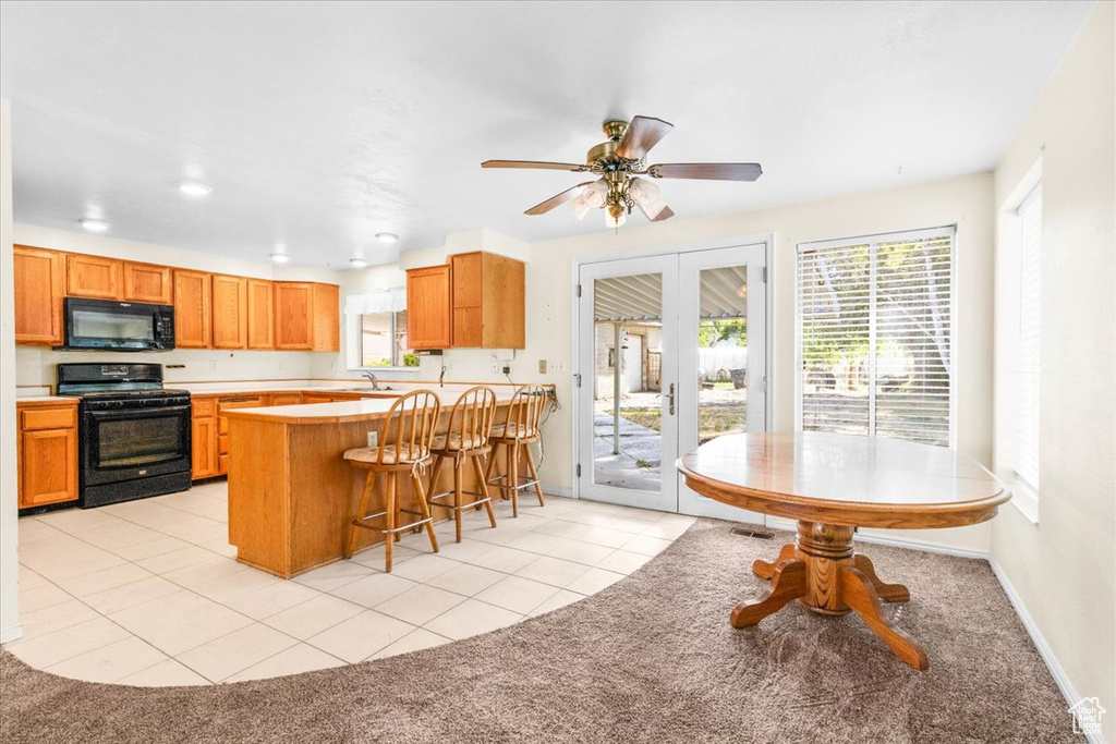 Kitchen with black appliances, light colored carpet, a kitchen breakfast bar, recessed lighting, and light countertops