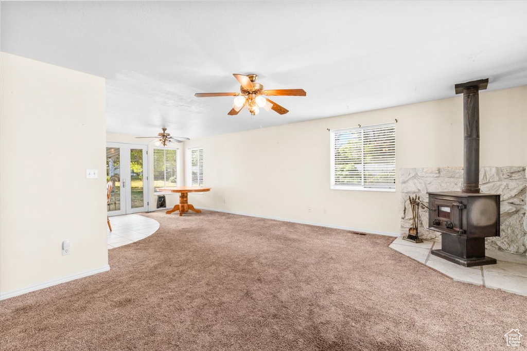 Unfurnished living room featuring carpet floors, a wood stove, a ceiling fan, and french doors