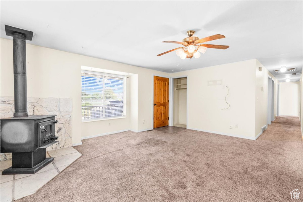 Unfurnished living room featuring a wood stove, carpet floors, and ceiling fan