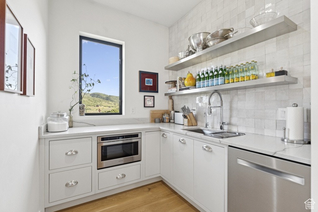 Kitchen with open shelves, decorative backsplash, stainless steel dishwasher, and white cabinets