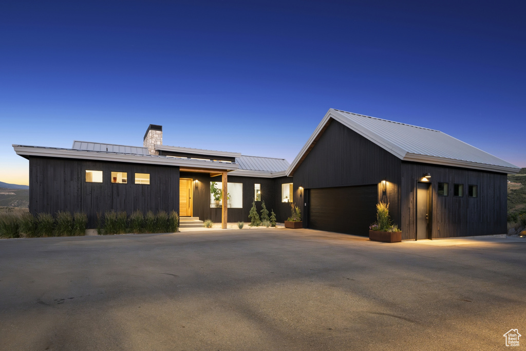 View of front of home with a metal roof, a chimney, driveway, an attached garage, and board and batten siding