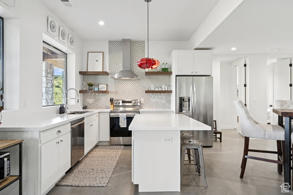 Kitchen with open shelves, stainless steel appliances, recessed lighting, a kitchen bar, and wall chimney exhaust hood