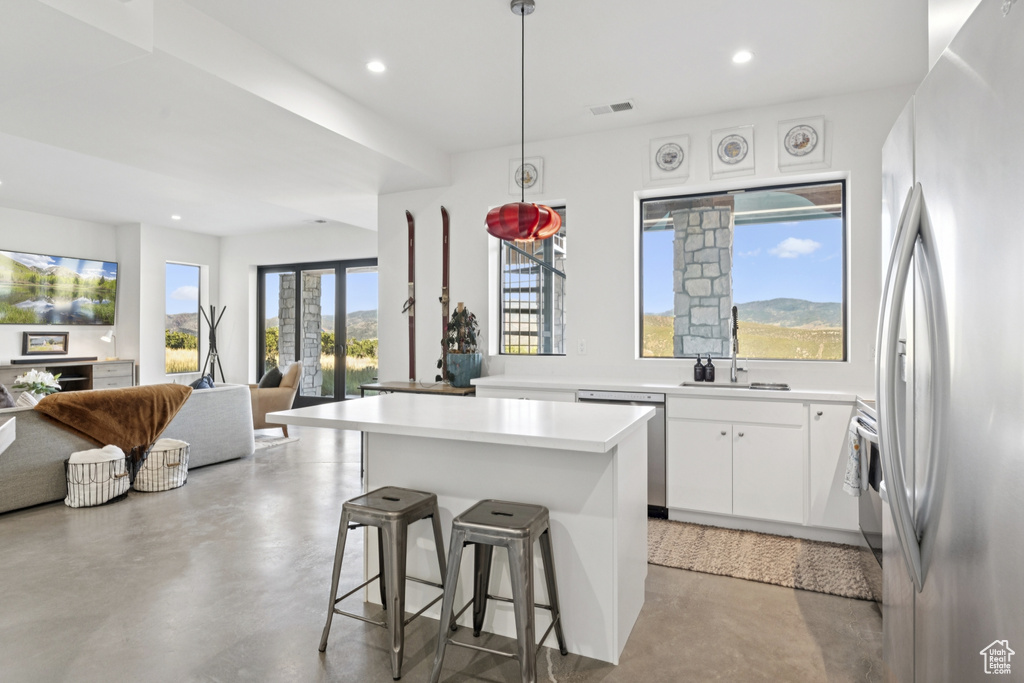 Kitchen featuring finished concrete floors, appliances with stainless steel finishes, a center island, recessed lighting, and a kitchen bar