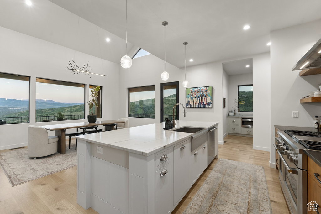 Kitchen featuring appliances with stainless steel finishes, light wood finished floors, an island with sink, light stone countertops, and recessed lighting