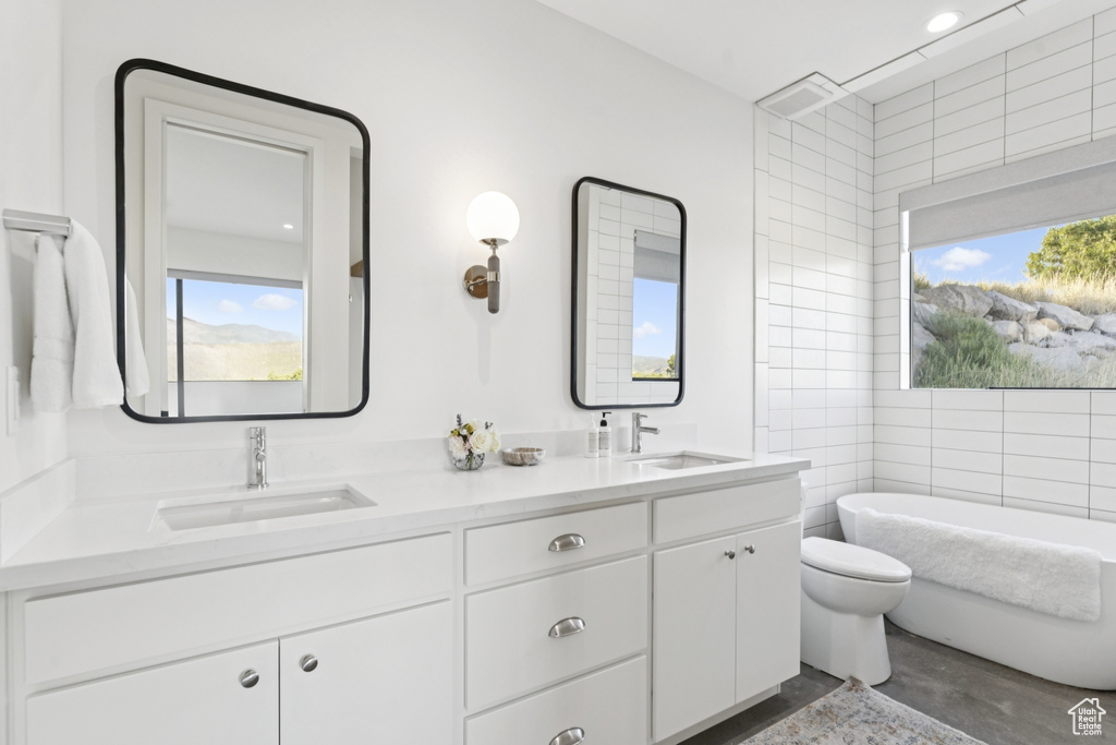 Full bath featuring plenty of natural light, a soaking tub, double vanity, and tile walls