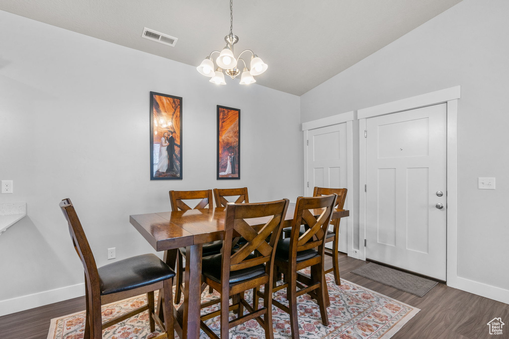Dining space with a chandelier, dark wood-style floors, and vaulted ceiling