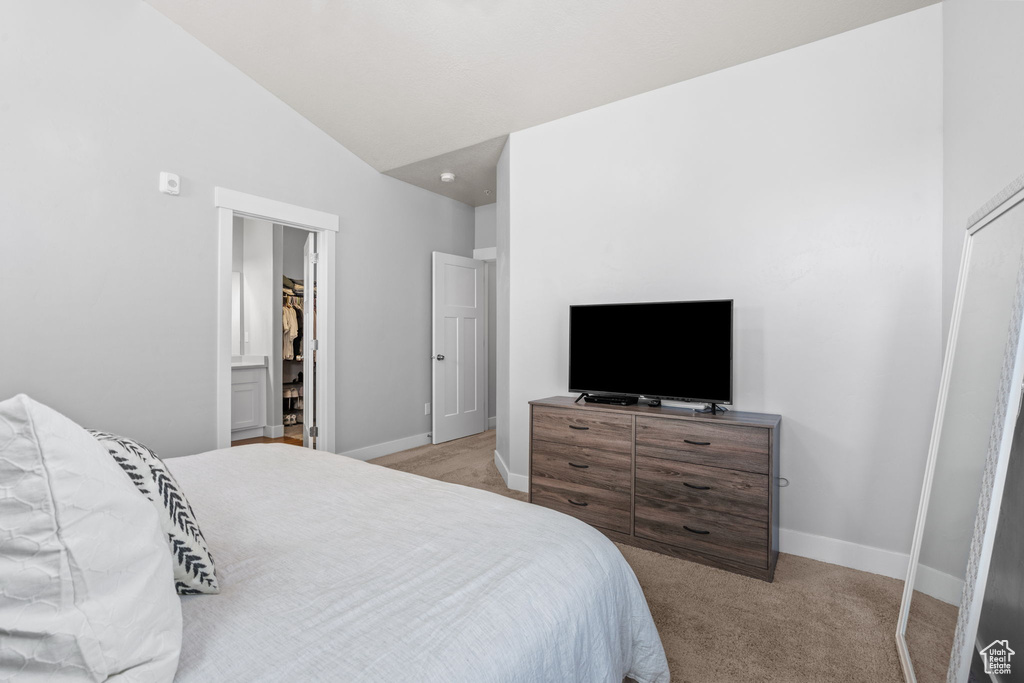 Bedroom featuring light colored carpet, lofted ceiling, and a walk in closet