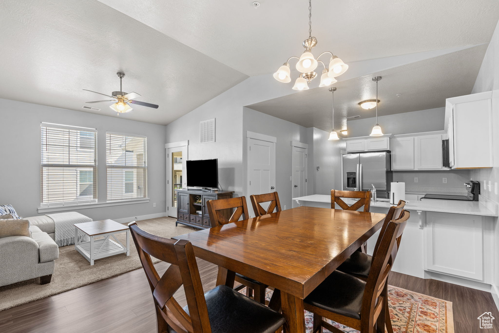 Dining area featuring vaulted ceiling, wood finished floors, ceiling fan, and a chandelier