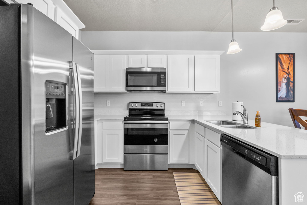 Kitchen with appliances with stainless steel finishes, a peninsula, white cabinets, dark wood-style flooring, and hanging light fixtures