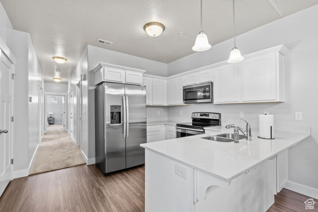 Kitchen featuring appliances with stainless steel finishes, a peninsula, wood finished floors, white cabinets, and a textured ceiling