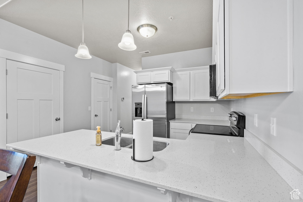 Kitchen featuring stainless steel appliances, white cabinets, light stone countertops, a peninsula, and decorative light fixtures