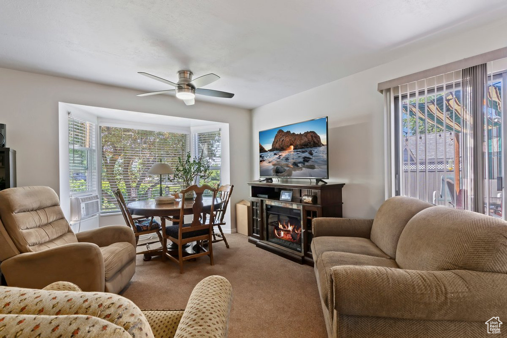 Living room featuring carpet flooring, a ceiling fan, plenty of natural light, and a glass covered fireplace