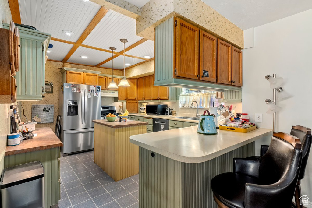 Kitchen featuring a peninsula, appliances with stainless steel finishes, dark tile patterned floors, light countertops, and a center island