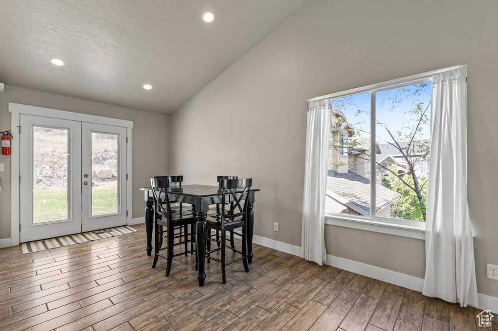 Dining space with french doors, healthy amount of natural light, wood finished floors, vaulted ceiling, and recessed lighting