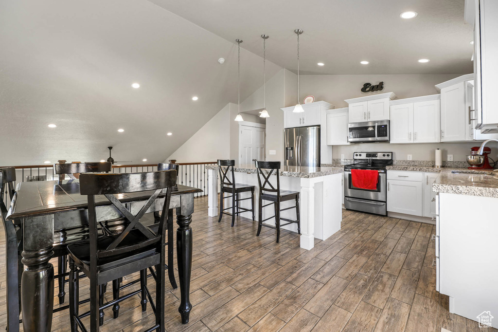 Kitchen with stainless steel appliances, a center island, wood finished floors, a breakfast bar, and white cabinetry