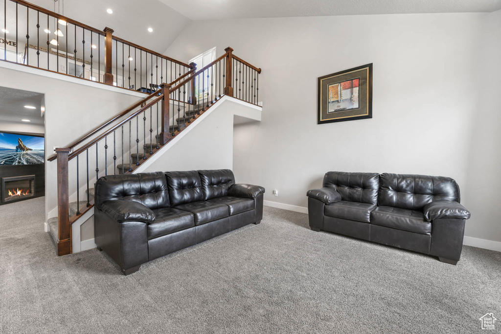 Living room with carpet flooring, high vaulted ceiling, stairway, a premium fireplace, and recessed lighting