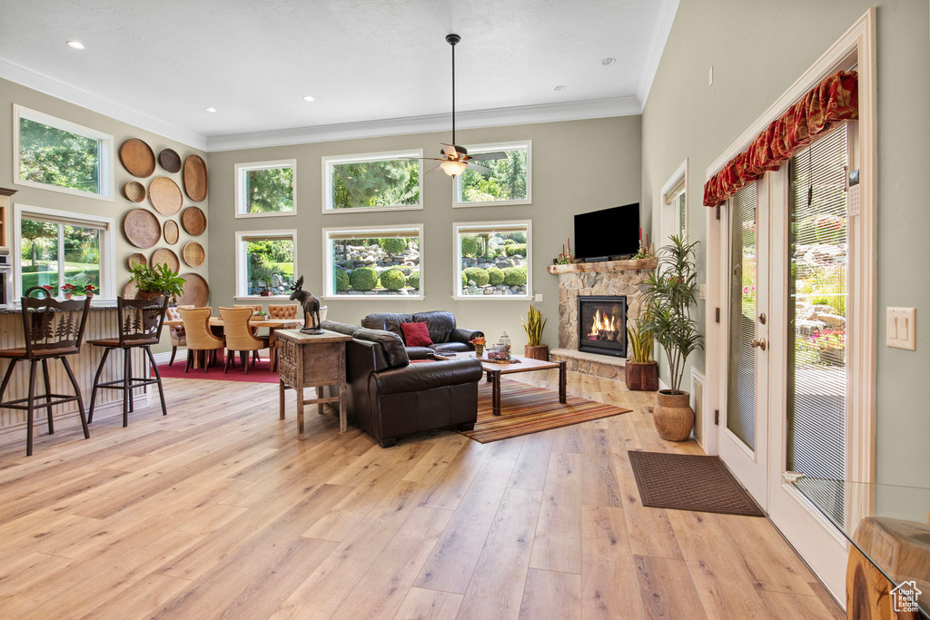 Living area with crown molding, a stone fireplace, light wood-type flooring, ceiling fan, and a towering ceiling