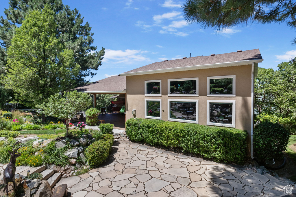 View of side of home featuring stucco siding, a patio area, and roof with shingles