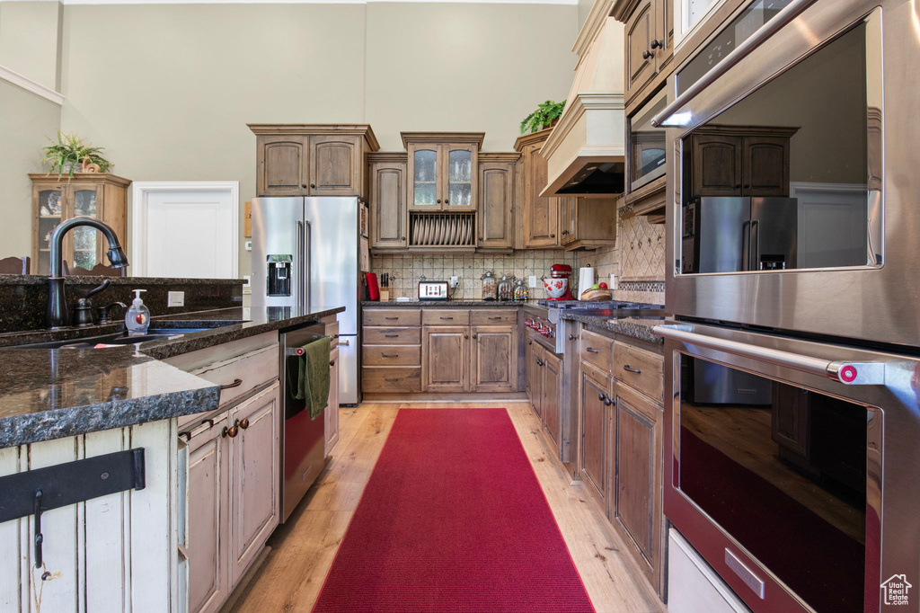Kitchen featuring stainless steel appliances, decorative backsplash, light wood-style flooring, a towering ceiling, and glass insert cabinets