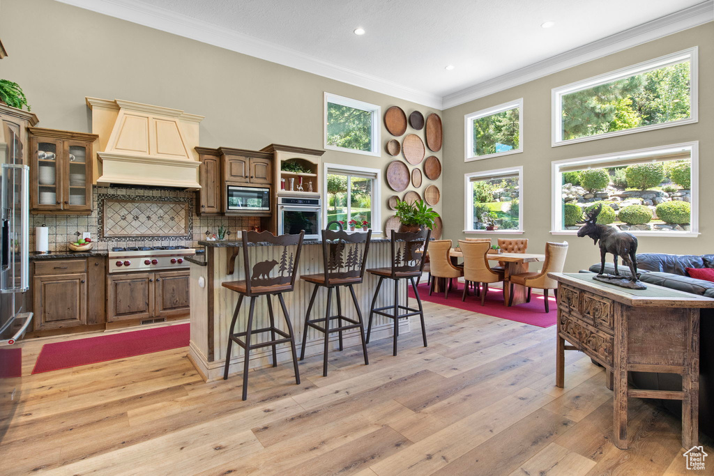 Kitchen featuring crown molding, a kitchen bar, light wood finished floors, appliances with stainless steel finishes, and decorative backsplash