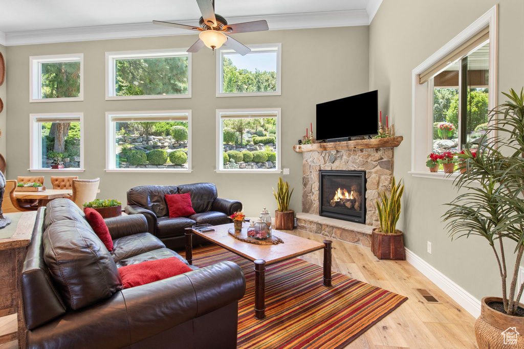 Living area featuring a ceiling fan, crown molding, wood finished floors, and a stone fireplace